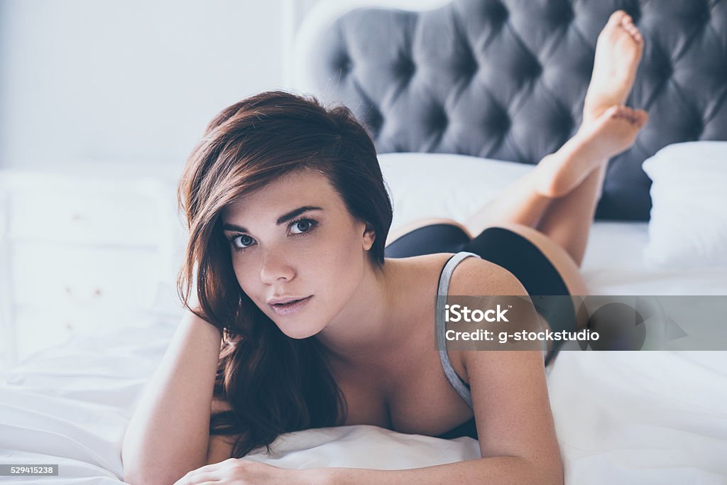 Seductive beauty in bed. Beautiful young woman in black lingerie looking at camera while lying on front in bed Bed - Furniture Stock Photo