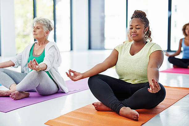 Release all your tension Shot of a group of women meditating indoors yoga class stock pictures, royalty-free photos & images