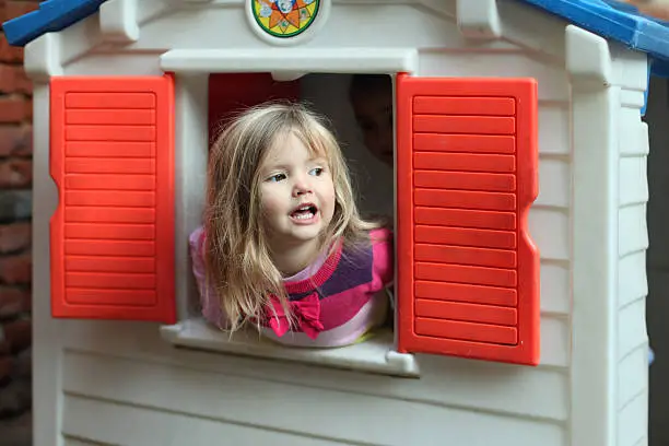 Little blond girl smiling through the window of kids playhouse