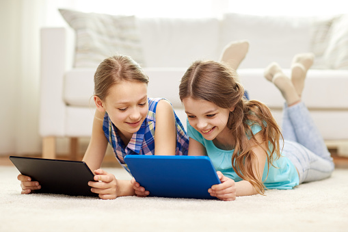 people, children, technology, friends and friendship concept - happy little girls with tablet pc computers lying on floor at home