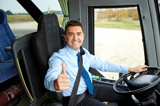 transport, tourism, road trip and people concept - happy driver driving intercity bus and snowing thumbs up