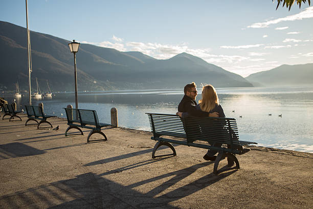 Lovely couple sitting on bench hugging at sunset watching the lake-Autumn