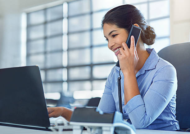 She makes multitasking look like a breeze Shot of a young businesswoman talking on the phone while using a laptop at work landline phone stock pictures, royalty-free photos & images