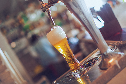 Full glass of beer under the faucet at bar. Focus on foreground.