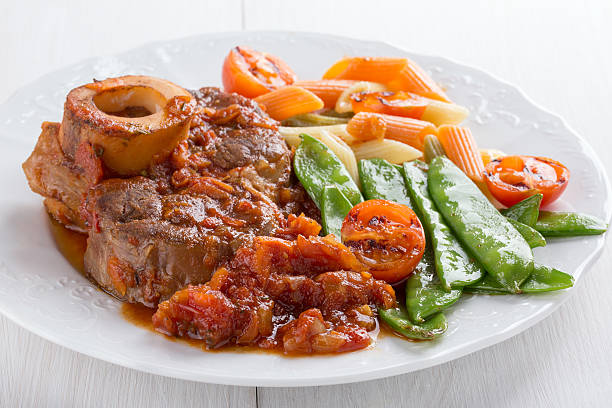 Ossobuco. Cross-cut veal shanks braised with vegetables. Ossobuco.Cross-cut veal shanks braised with vegetables. Served with garnish (penne, pea pods and cherry tomatoes). ossobuco stock pictures, royalty-free photos & images