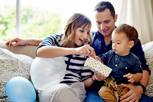 Shot of an adorable little boy opening presents with his mother and father on his first birthday