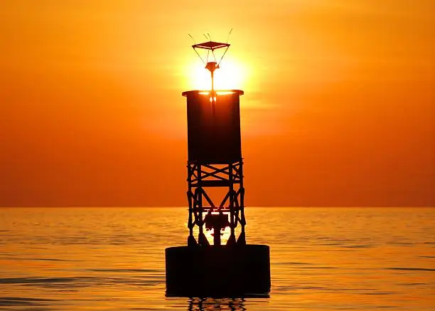 In Chesapeake Bay, Virginia, an aid to navigation (buoy) is silhouetted by the rising sun.