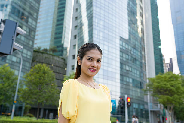 Asian woman expressing confidence Attractive long hair Asian woman looking at camera with toothy smile, expressing confidence, with business district in background, shot with wide angle lens with shallow depth of field to blur out background details. Maid in Singapore stock pictures, royalty-free photos & images