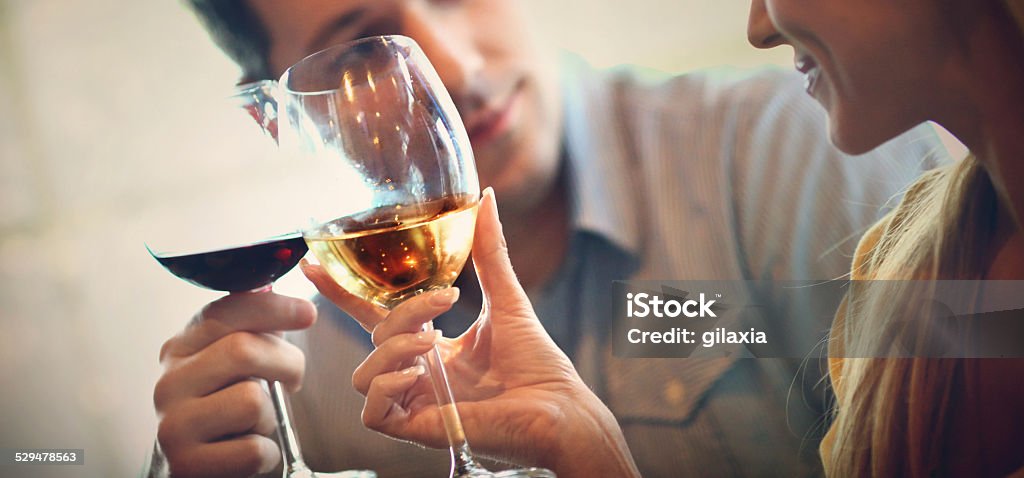 Wine drinkers. Unrecognizable young to middle aged couple drinking wine on a date.Sitting side by side and whispering sweet words to each other.The woman is drinking white wine and he's drinking red.She's blond,wearing yellow long sleeved shirt and he's wearing casual blue shirt. Wine Stock Photo