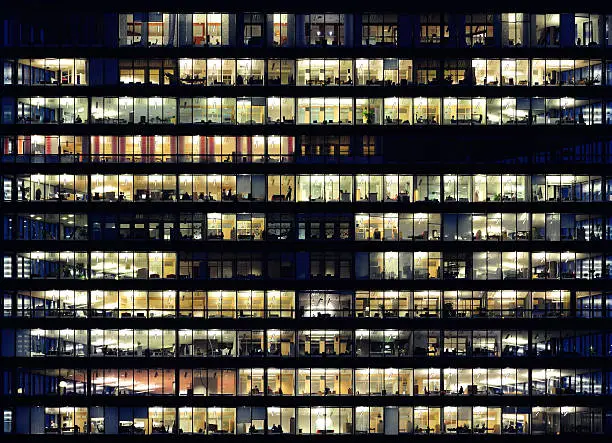 Photo of Workers working late. Office windows by night.