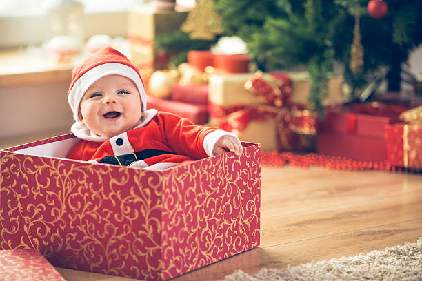 Christmas baby Cute little baby boy in Santa hat sitting inside of the red gift box next to the Christmas tree. babies only photos stock pictures, royalty-free photos & images