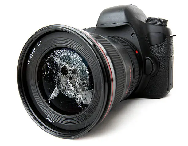 Modern DSLR camera with a smashed lens on white background
