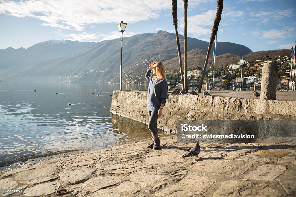 Young woman near lake looking at view on sunny day-Autumn Young woman near the lake Maggiore in Ascone-Switzerland looking at the view.Sunny day in Autumn. Adult Stock Photo