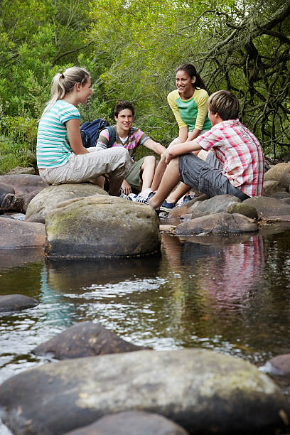 istock Teenagers Sitting On Stones By River In Forest 529557885