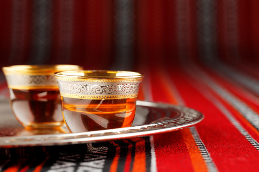 A tray of Arabian tea cups is placed on Arabian woven fabric. Tea symbolise Arabian hospitality