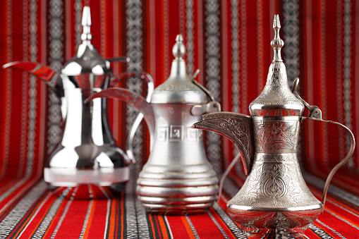 Three ornate Dallah are placed on traditional red fabric from the Middle East. Dallah is a metal pot for making tea and coffee