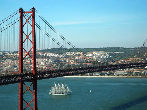 Lisbon, Portugal: city skyline and the 25 de Abril bridge over the estuary of the river Tagus - a four masted sailing ship passes under the bridge - formerly known as Salazar Bridge, after prime minister Antonio de Oliveira Salazar, later renamed after the 1974 coup d'etat - photo by M.Torres