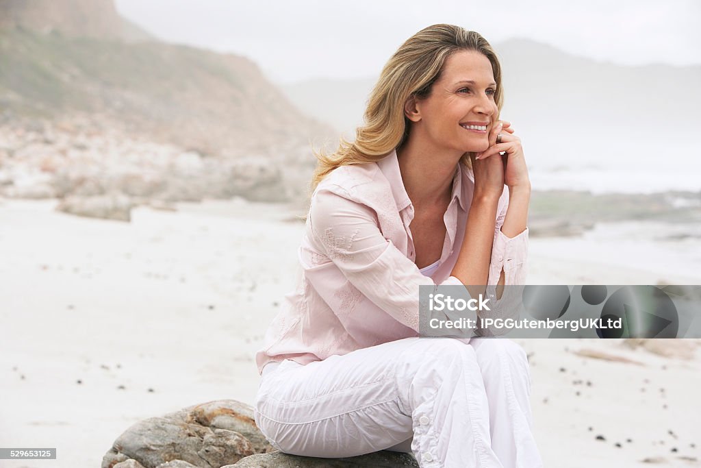 Happy Woman Relaxing On Rock At Beach Happy woman looking away while relaxing on rock at beach Adult Stock Photo