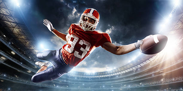 Football player catches a ball Professional football player catches a ball. The action takes place on professional stadium. The player wears unbranded sports uniform. There is artificial light on stadium together with sunlight. exhilaration photos stock pictures, royalty-free photos & images