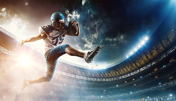 Football player runs with the ball Professional football player (Running Back) runs with the ball. The action takes place on professional stadium. The player wears unbranded sports uniform. There is artificial light on stadium together with sunlight. american football sport stock pictures, royalty-free photos & images