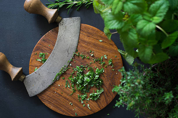 Aromatic herbs chopped with mezzaluna knife Aromatic herbs chopped with mezzaluna knife on wooden cutting board mezzaluna stock pictures, royalty-free photos & images