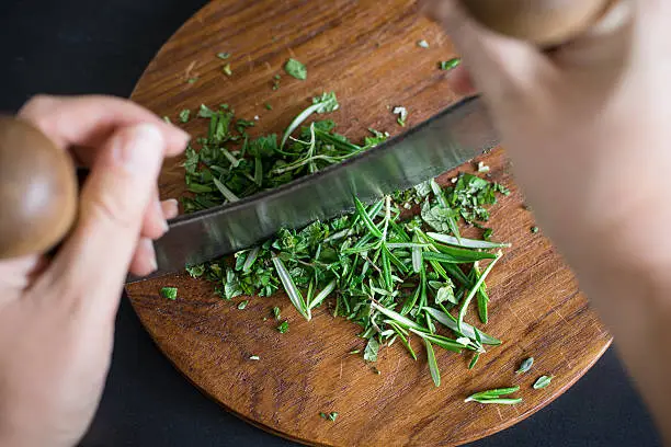 Photo of Chopping aromatic herbs with italian mezzaluna knife. Selective focus.