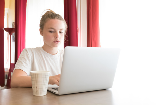 Beautiful girl using her laptop on the breakfast table in her apartment.