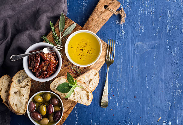 Mediterranean snacks set. Olives, oil, herbs and sliced ciabatta bread Mediterranean snacks set. Olives, oil, herbs and sliced ciabatta bread on yellow rustic oak board over painted dark blue background, top view, copy space greek food stock pictures, royalty-free photos & images