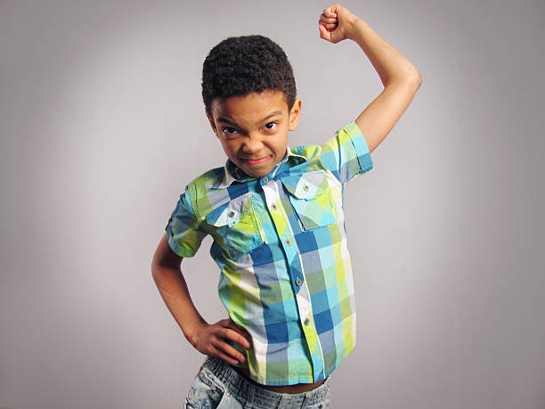 A boy threatening with his fist over grey background. Vertical Shot.