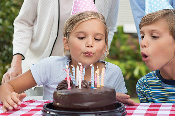 Girl blowing out the candles Young girl blowing out birthday candles of chocolate cake. Portrait of young girl celebrating birthday with family and brother. Brother helping sister blow candles on birthday cake. birthday wishes for daughter stock pictures, royalty-free photos & images