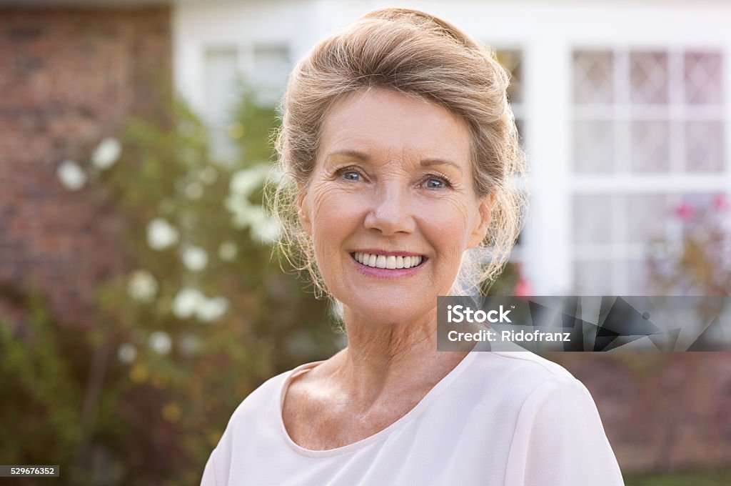 Smiling senior woman Happy senior woman standing outside her house. Content woman smiling and looking at camera. Portrait of cheerful old grandmother relaxing outside the house. Senior Women Stock Photo