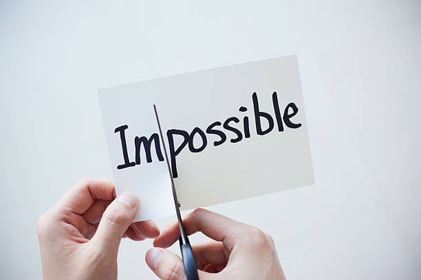 Using Scissors Cut the Word on Paper Impossible Become Possible Close-up of hand using scissors cutting the word on paper, Impossible become Possible. impossible possible stock pictures, royalty-free photos & images