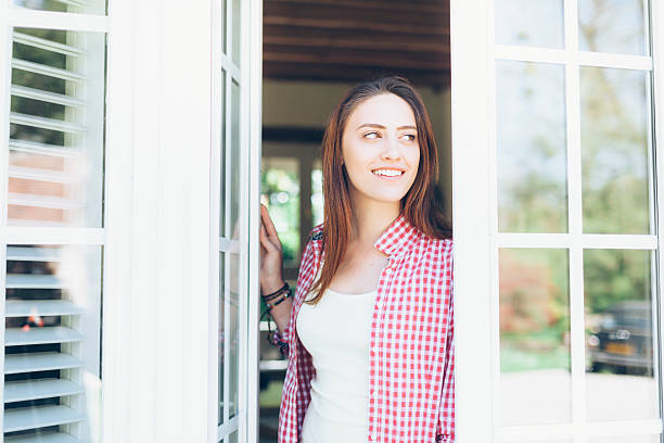 joven mujer mirando a través de la ventana - window sun sunlight vertical fotografías e imágenes de stock