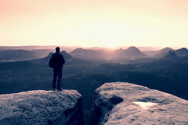 istock Tourist with backpack and poles on rock looking into sun 529680764