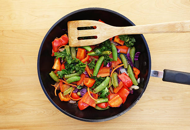 Colorful stir fry in a skillet. Ingredients include sugar peas, red bell pepper, chopped kale, slivers of carrots, onions, and bits of chopped red cabbage. Healthy vegetable meal.