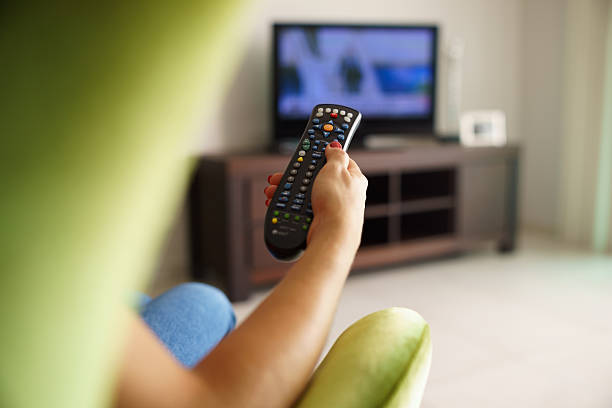istock Woman on sofa watching tv changing channel with remote 529689367