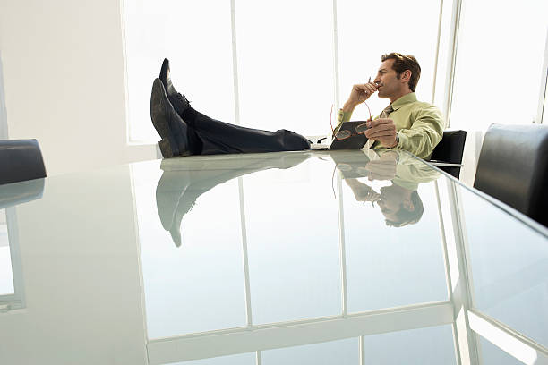 Studio shot isolated on a white background of a young businessman sitting lounging on an office chair, looking at the camera with a thumb on lips and making face.