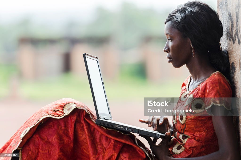 Education for Africa: Technology Symbol African Woman Studying Learning Lesson Street Shot of an African Ethnicity young woman working on business holding her technology item computer in a university in Bamako, Mali. Blurred background. University high school environment.  Africa Stock Photo