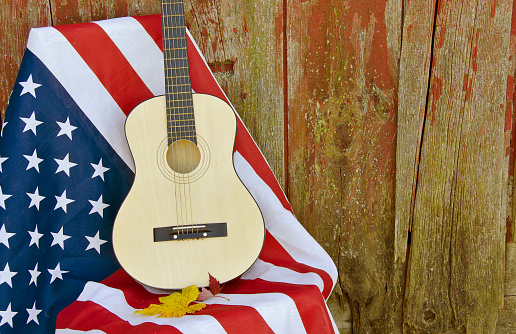 Guitar on an American flag by old barn with fall leaves.