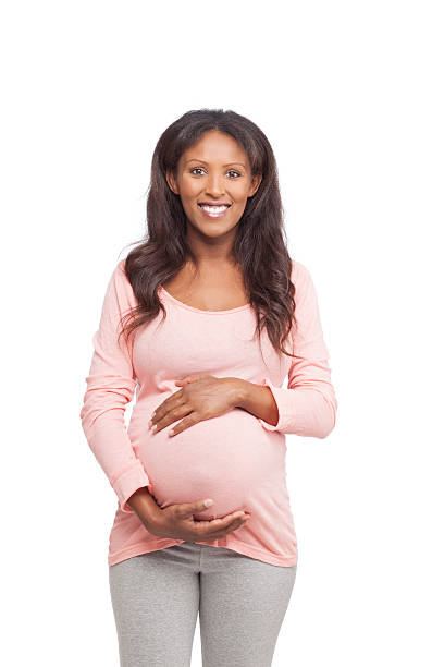 Studio shot of 8 months pregnant woman stroking her belly and looking over the camera. Cut out image. with copy space.