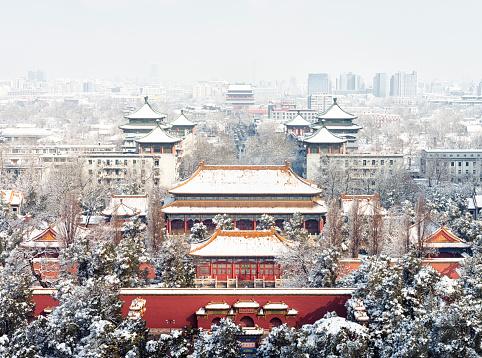 Snow over the skyline of Beijing, looking north, with the trees and buildings of Jingshan Park in the foreground, the Drum Tower (Gǔlóu) in the distant centre of the image, and modern commercial towers beyond.