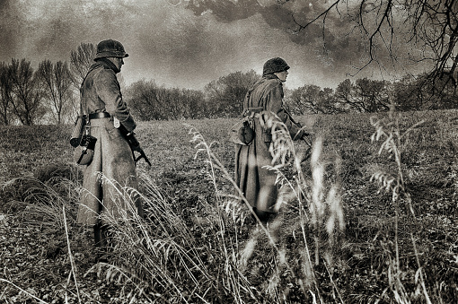 Two WWII German era Soldiers on patrol together.  Aged photograph.  Uniforms, guns, equipment, helmets, boots all authentic for the period.  Grain, crackle, scratches, dust. Copy Space.