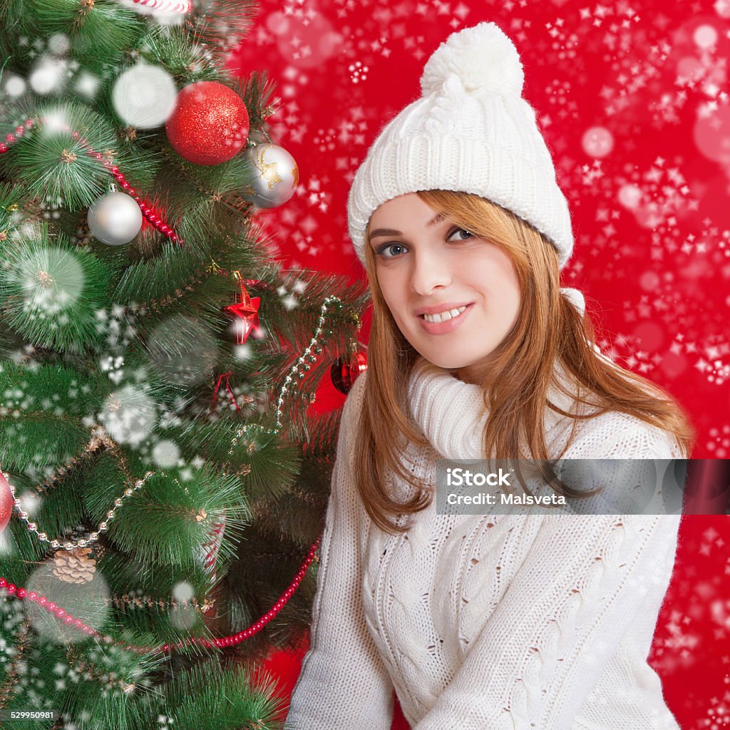 Beautiful young woman  near Christmas tree Beautiful young woman  near Christmas tree on red background. In white knitted cap and sweater. Adult Stock Photo