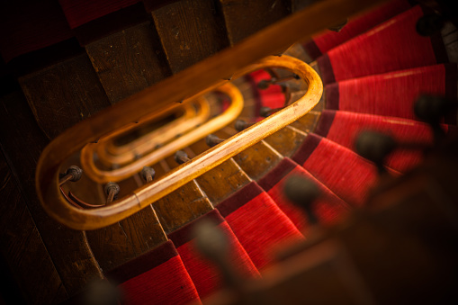 View down a wooden spiral staircase with a red carpet runner, in an old Parisian apartment building.