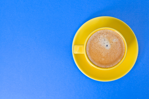 Coffee in a yellow cup on a blue background with copy space