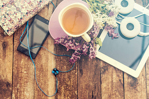 still life with tea cup on a wooden table still life with tea cup and the contents of a work space composed. Different objects on wooden table. tablet,phone with headphones and spring flowers pink tea stock pictures, royalty-free photos & images