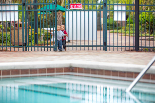 Twin little boys try to enter an unlocked swimming pool Terrible two's times two. Twin boys are attempting to enter an unlocked gate at a large swimming pool at a resort. Shot with Canon 5D Mark 3 rm pool gate stock pictures, royalty-free photos & images