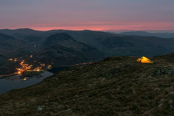 Glowing backpacking tent on side of mountain overlooking valley.