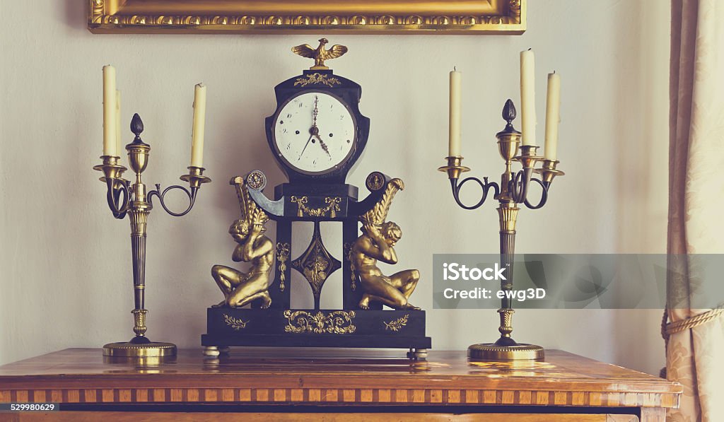 Retro clock Antique chest of drawers with vintage grandfather clock and candlesticks in front of a window in a living room. Grandfather Clock Stock Photo