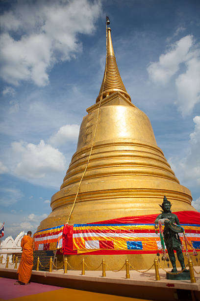 Bangkok, Thailand - November 28, 2013. A Thai monk prays in front of the golden chedi at Wat Saket.
